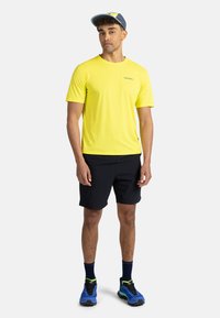 Ljusgul sportt-shirt, svarta shorts, i kombination med blå skor och marinblå keps. Minimalistisk design med logotyp på tröjan.