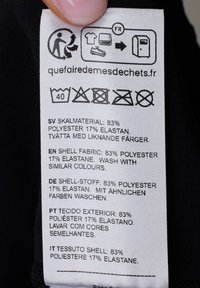 Verzorgingslabel op stof; witte tekst op een zwarte achtergrond. Inhoud: 83% polyester, 17% elastaan; meertalige verzorgingsinstructies inbegrepen.