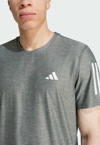 Camiseta atlética gris fabricada con material que absorbe la humedad, con un logo triangular blanco en el pecho y tres líneas blancas en la manga.