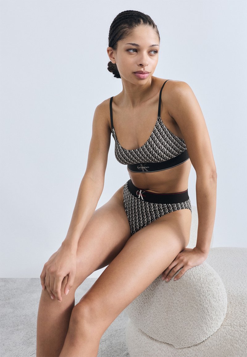 Σετ εσωρούχων σε μαύρο και άσπρο με μοτίβο, που περιλαμβάνει ένα μπραλέ και σλιπ με ψηλή μέση, με λεπτές τιράντες και λογότυπο. Ορατή μαλακή υφή.