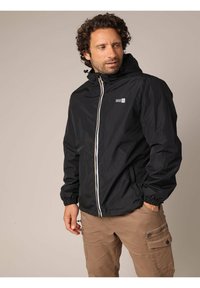 Zwarte waterdichte jas met een rits aan de voorkant, elastische manchetten en een capuchon. Voorzien van een klein logo-opdruk op de borst en een witte ritsaccent.