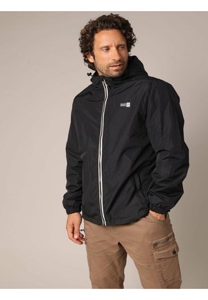 Veste imperméable noire avec fermeture éclair à l'avant, manches élastiques et capuche. Présente un petit logo sur la poitrine et un accent de fermeture éclair blanche.