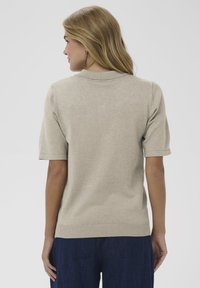 Béžový pletený polo s krátkym rukávom, s rebrovaným golierom a lemom, hladkou textúrou a voľným strihom, so jednoduchým dizajnom bez vzorov.