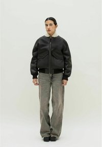 Schwarze Lederbomberjacke mit einem Kunstfellkragen, zwei frontalen Taschen, gerippten Bündchen und hellen, geraden Jeans, kombiniert mit Plateauschuhen.