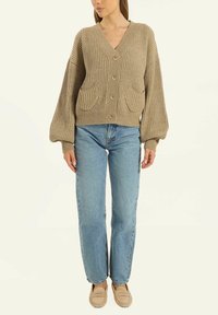 Beige gerippter Strick-Cardigan mit V-Ausschnitt, vorderen Knöpfen und zwei großen aufgesetzten Taschen. Hat voluminöse Ärmel und ein verkürztes Design.