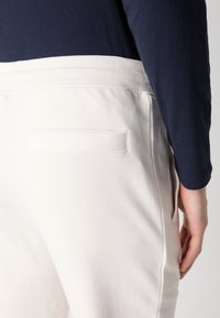Joggers de mezcla de algodón blanca con una cinturilla acanalada, que presentan un bolsillo trasero y una textura suave, vistos desde el lado izquierdo.