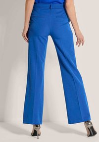 Blauwe wijde broek heeft een op maat gemaakt ontwerp met een gladde textuur en achterzakken. Gekleed met metallic hoge hakken.