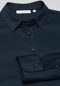 Camicia button-up blu scuro con colletto classico, design aderente, texture liscia, leggera lucentezza e due bottoni scuri sulla patta.