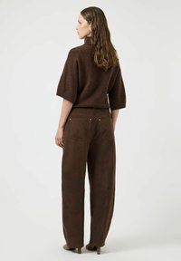 Maglione marrone lavorato a maglia con maniche corte, abbinato a pantaloni ampi in camoscio marrone scuro. Caratterizzato da tasche posteriori e un design testurizzato sottile.