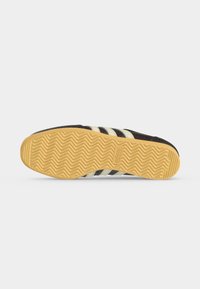 Μαύρη και λευκή σόλα αθλητικού παπουτσιού Adidas με πατούρα από καουτσούκ σε ζιγκ-ζαγκ και λογότυπο Adidas χαραγμένο στο κέντρο.