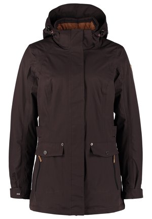 Person trägt eine schwarze Kapuzenjacke, weißes ärmelloses Oberteil, olivgrüne Hose und graue Sneakers, geht mit einer Hand in der Tasche.