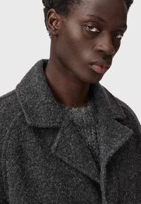 Mørkegrå uldblandingsfrakke med en spids revers og tekstureret overflade. Har skjulte lukninger og en hyggelig strikket sweater underneath.