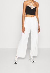 Černý zkrácený halter top s bílými akcenty a centrálním kroužkem, spárovaný s volnými bílými kalhotami a šedými teniskami.