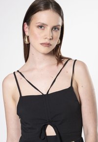 Top negro sin mangas con tirantes finos, que presenta un detalle de nudo en el frente y un corte en forma de llave. Tejido liso con textura mínima.