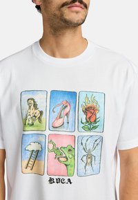 T-shirt bianco in cotone con un design grafico colorato composto da sei pannelli che raffigurano un cavallo, un tacco alto, una rosa, una nuvola, una rana e un ragno.