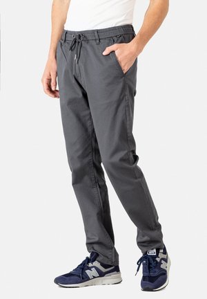 Gray chinos with an elastic waistband and adjustable drawstring. Features side pockets and a slim fit. Worn with dark blue sneakers.