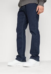 Marinblå denimjeans med rak passform, subtila sömnadsdetaljer och i kombination med vita sportskor.