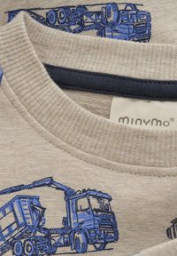 Beige skjorta med blå lastbilsillustrationer, ribbade rundhals, mjukt material och en liten etikett med "minymo"-logotyp.