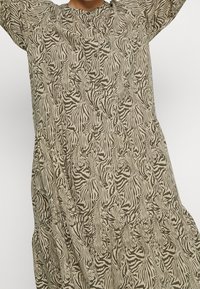 Abito a maniche lunghe, lungo fino al ginocchio, beige con motivo a zebre nere, caratterizzato da una scollatura rotonda e una vita arricciata per aggiungere texture.