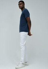 Camiseta de manga corta en azul marino con un bolsillo en el pecho, combinada con pantalones ajustados blancos y zapatillas blancas. Diseño minimalista y aspecto informal.