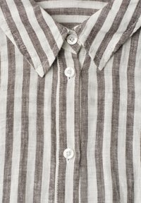 Chemise à col avec des rayures verticales marron et blanches, comportant trois boutons blancs sur la patte de boutonnage avant.