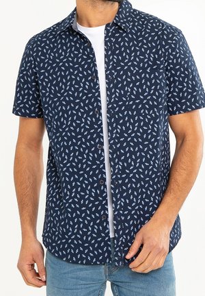 Korte mouw navy shirt met een witte bloemenpatroon; met knopen aan de voorkant; gedragen over een wit T-shirt; gemaakt van ademend materiaal.