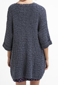 Mörkblå stickad tröja med lös, öppen väv, trekvartslånga ärmar och ribbade muddar. Har sidofickor och en avslappnad passform.