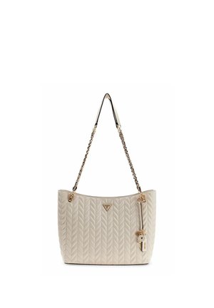 Sac à main matelassé beige avec des chaînes à maillons dorés et un pendentif suspendu, arborant un petit logo de marque triangulaire à l'avant.