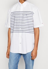 Vitt kortärmat skjorta med horisontella marinblå ränder, knapp-down krage och bröstficka. Inkluderar Tommy Hilfiger-logotyp accenter.