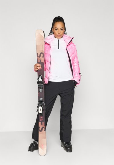 Ροζ φουσκωτό μπουφάν, λευκό μακρύ μανίκι, μαύρο παντελόνι σκι, κρατώντας ένα σκι με μπιντέδες. Μαύρα μποτάκια σκι με γκρι λεπτομέρειες.