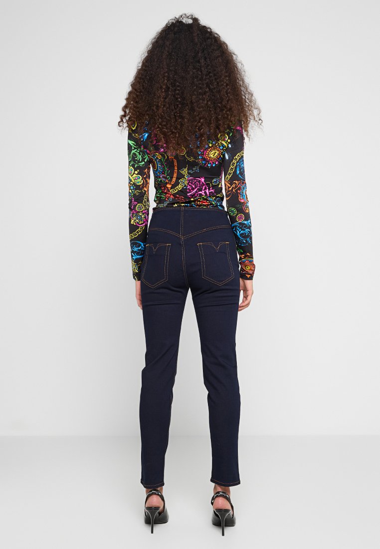 Kolorowa bluzka z długim rękawem i skomplikowanymi wzorami, w połączeniu z ciemnoniebieskimi dżinsami. Dżinsy posiadają kieszenie i kontrastowe przeszycia.