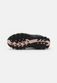 Semelle de chaussure de randonnée noire avec des crampons profonds et des accents rose clair, conçue pour la traction sur un terrain accidenté.