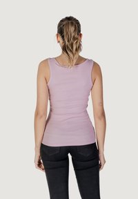 Top aderente rosa chiaro con scollo rotondo, texture a coste e spalline larghe, abbinato a jeans neri a vita alta.