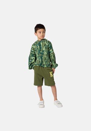 Green patterned hoodie with a hood, paired with olive shorts featuring a yellow letter 'K'. The child wears white sneakers.
