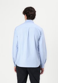 Chemise à manches longues bleu clair en tissu doux, avec un col standard, un plis au dos, des poignets boutonnés et un ourlet arrondi.