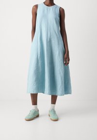 Vaaleansininen hihaton pellavamekko, jossa on rento siluetti, ulottuen kyynärpäähän asti, yhdistettynä mintunvihreisiin lenkkareihin ja valkoisiin nilkkasukkiin.