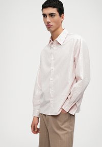 Prúžkovaná košeľa na gombíky v svetloružovej a bielej farbe, s dlhými rukávmi, klasickým golierom a mierne voľným strihom.