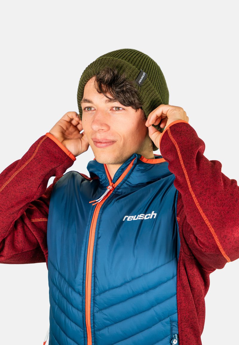 Green ribbed beanie worn by a person with dark hair. The individual is in a blue and red jacket with orange accents.
