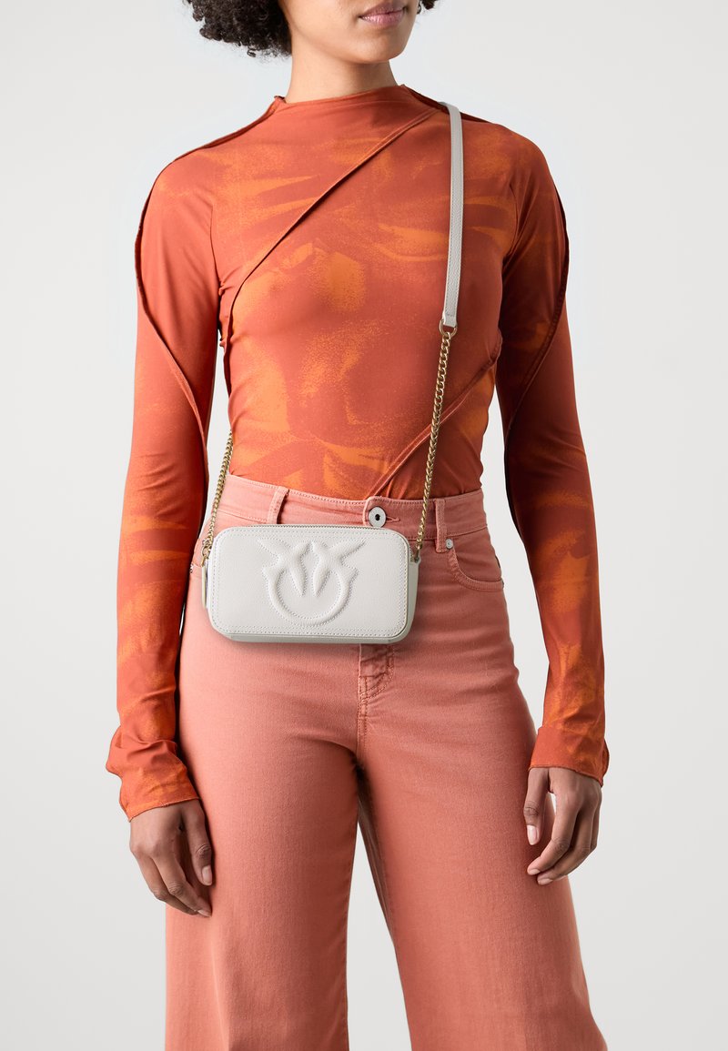 Crossbody bag in soft white leather, featuring embossed floral design, chain strap, rectangular shape, and smooth texture.