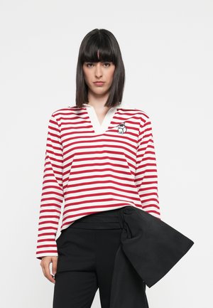 Red and white striped long-sleeve top with a V-neck and an embroidered graphic. Paired with black pants featuring a draped accent detail.