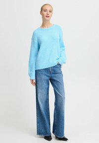 Maglione lavorato a maglia azzurro chiaro con una vestibilità comoda e scollo a coste, abbinato a jeans in denim a vita alta e gamba larga e scarpe nere a punta.