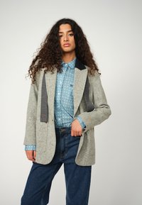 Gray tweed blazer with contrasting dark collar, paired with a light blue patterned shirt and high-waisted blue jeans.
