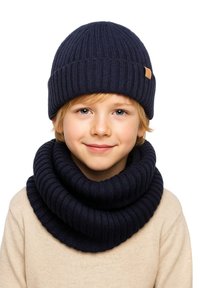 Navy knitted beanie with ribbed texture, paired with a matching ribbed infinity scarf, worn over a beige sweater.