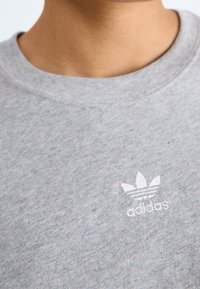 Felpa grigia in misto cotone con colletto rotondo. Presenta un logo Adidas ricamato bianco sul petto.