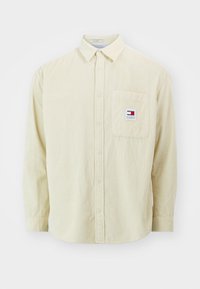 Camisa de pana amarillo claro con cuello abotonado, bolsillo frontal y pequeño parche de logo. Presenta una textura acanalada vertical.