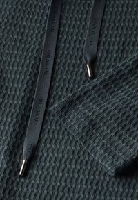 Texturiertes dunkelblaues Gewebe mit einem Gittermuster, ausgestattet mit schwarzen Kordeln und metallischen Akzenten. Glatte, gewebte Textur und maßgeschneiderte Kanten.