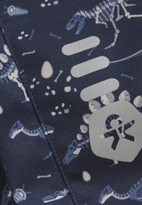 Marineblauer Stoff mit einem Muster aus Dinosaurier-Skeletten und Fossilien in hellen Farben, verziert mit einem silbernen Logo und Textakzenten.