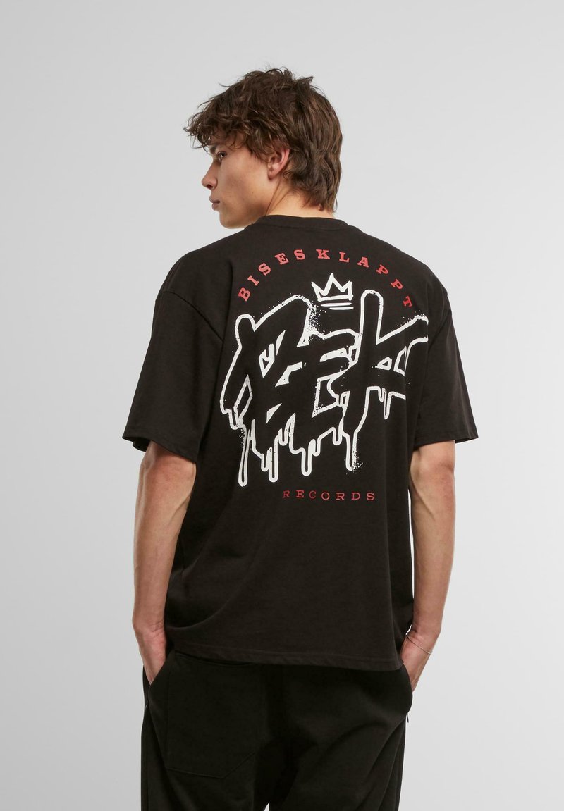 Juodas per didelis marškinėliai su dideliu baltu ir raudonu graffiti stiliaus logotipu nugarėlėje, su tekstu "Bisesklappt Records."