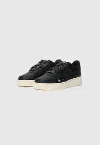 Une paire de baskets basses noires avec des semelles blanches, des lacets multicolores et de petits logos swoosh multicolores sur les côtés.