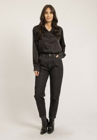 Chemise noire en satin à boutons, jean sombre taille haute en denim et bottines noires. Présente une texture lisse et une coupe ajustée.
